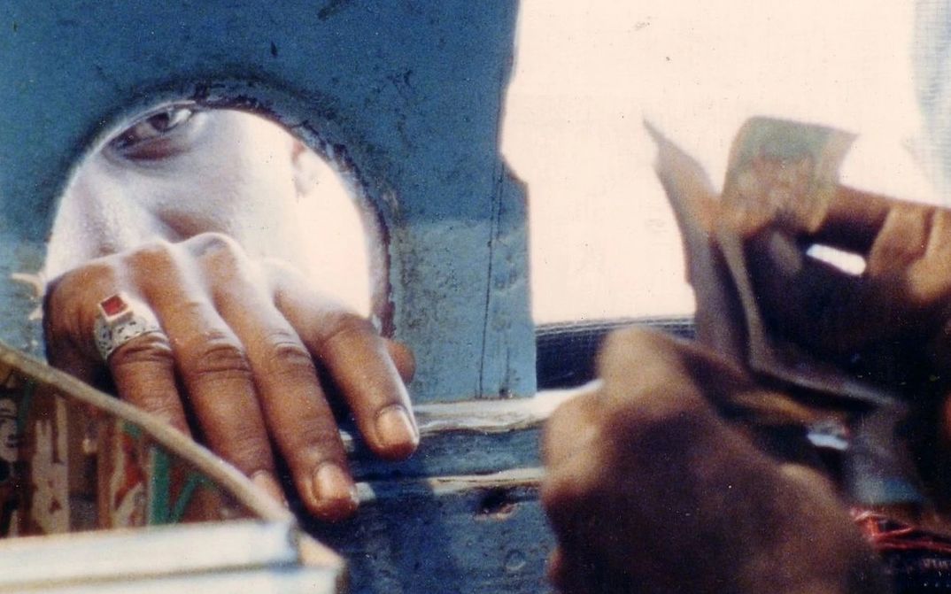 Filmstill aus KUMAR TALKIES: Aus dem Inneren eines Kassenhauses. Von außen sieht man das Gesicht einer Person, die soeben Geld hineingereicht hat.