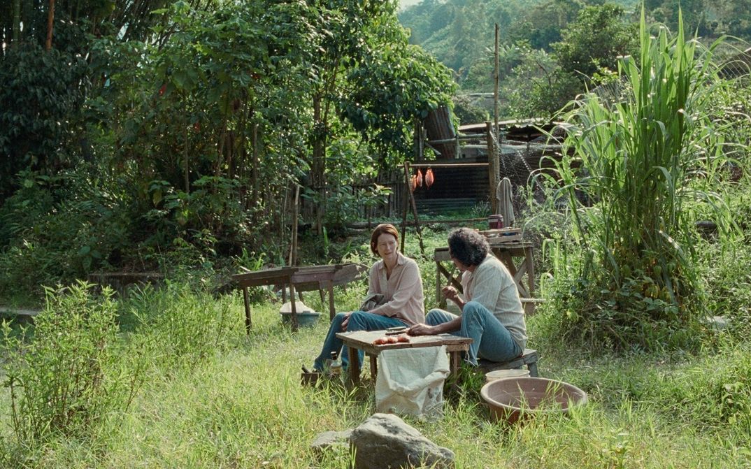  Film still from MEMORIA: Two people sitting in a lush green garden.