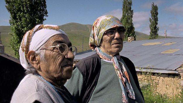 Still from the film "Dilim dönmüyor – Meine Zunge dreht sich nicht" by Serpil Turhan. Two old women standing on the village street in front of a adobe house. 