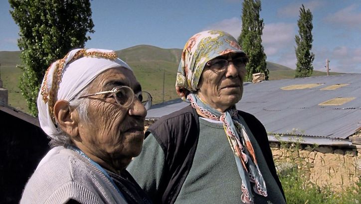 Still from the film "Dilim dönmüyor – Meine Zunge dreht sich nicht" by Serpil Turhan. Two old women standing on the village street in front of a adobe house. 