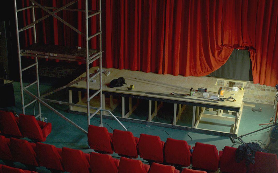Film still from CINÉMA LAIKA: View of a movie theater under construction. You can see the red screen and red chairs, a stage is being built.