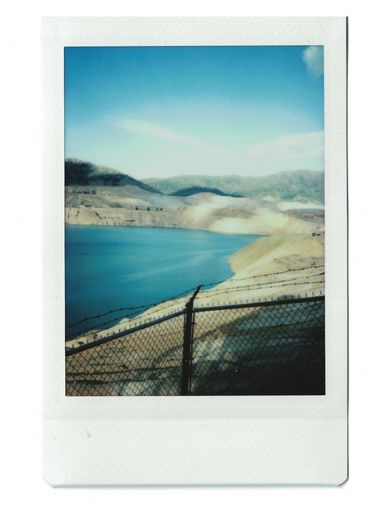 Polaroid of a reservoir, seen over a chain-linked fence.