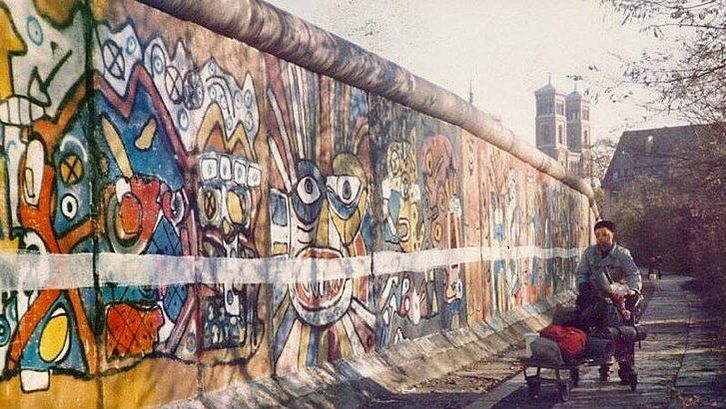 Filmstill aus STRICHE ZIEHEN: Zu sehen ist ein Stück der Berliner Mauer von westlicher Seite, sie ist bemalt und zusätzlich horizontal mit einer weißen Linie versehen.