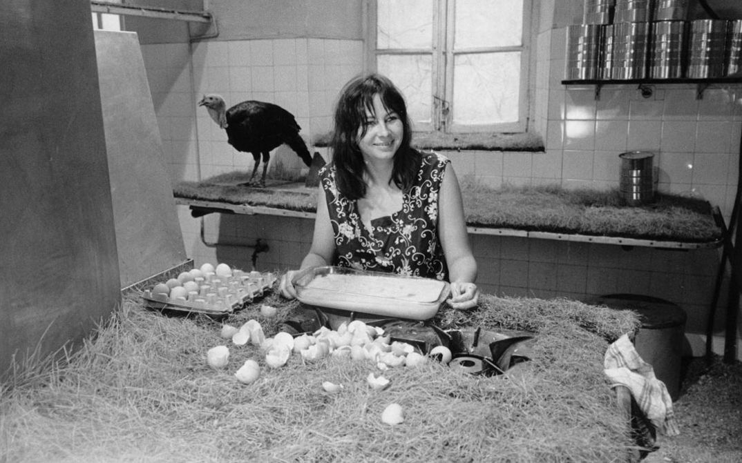 Filmstill aus 7 P., CUIS., S.DE B... À SAISIR. Eine Frau sitzt in einer einfachen Küche, vor sich eine Menge aufgeschlagener Eier. Im Hintergrund ist ein Truthahn zu sehen.