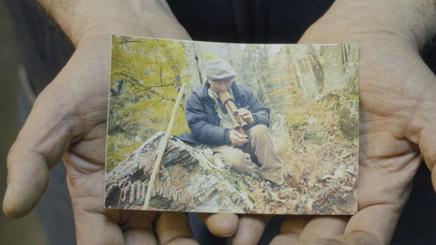 Film still from CANONE EFFIMERO by Gianluca De Serio and Massimiliano De Serio. The image shows a close-up of a photograph of a person in the forest, held by two hands.