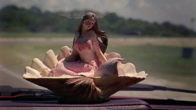 Filmstill aus NE CROYEZ SURTOUT PAS QUE JE HURLE: Auf dem Armaturenbrett eines Autos steht eine Plastikmuschel mit einer Meerjungfrau.