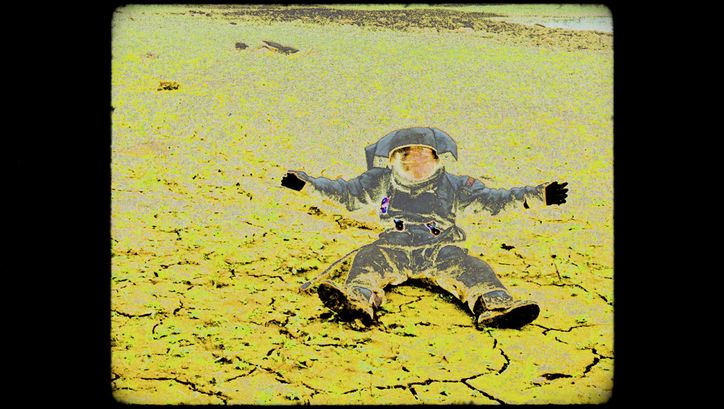 Ein Bild von einem sitzenden Astronauten mit ausgebreiteten Armen im Raumanzug vor karger Landschaft; die Aufnahme sieht wie eine Negativkopie eines analogen Filmbildes aus mit sichbaren Bildstörungen.