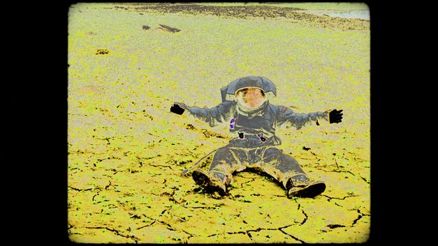 Ein Bild von einem sitzenden Astronauten mit ausgebreiteten Armen im Raumanzug vor karger Landschaft; die Aufnahme sieht wie eine Negativkopie eines analogen Filmbildes aus mit sichbaren Bildstörungen.