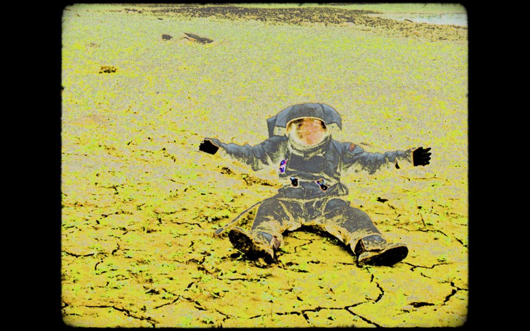 Ein Bild von einem sitzenden Astronauten mit ausgebreiteten Armen im Raumanzug vor karger Landschaft; die Aufnahme sieht wie eine Negativkopie eines analogen Filmbildes aus mit sichbaren Bildstörungen.
