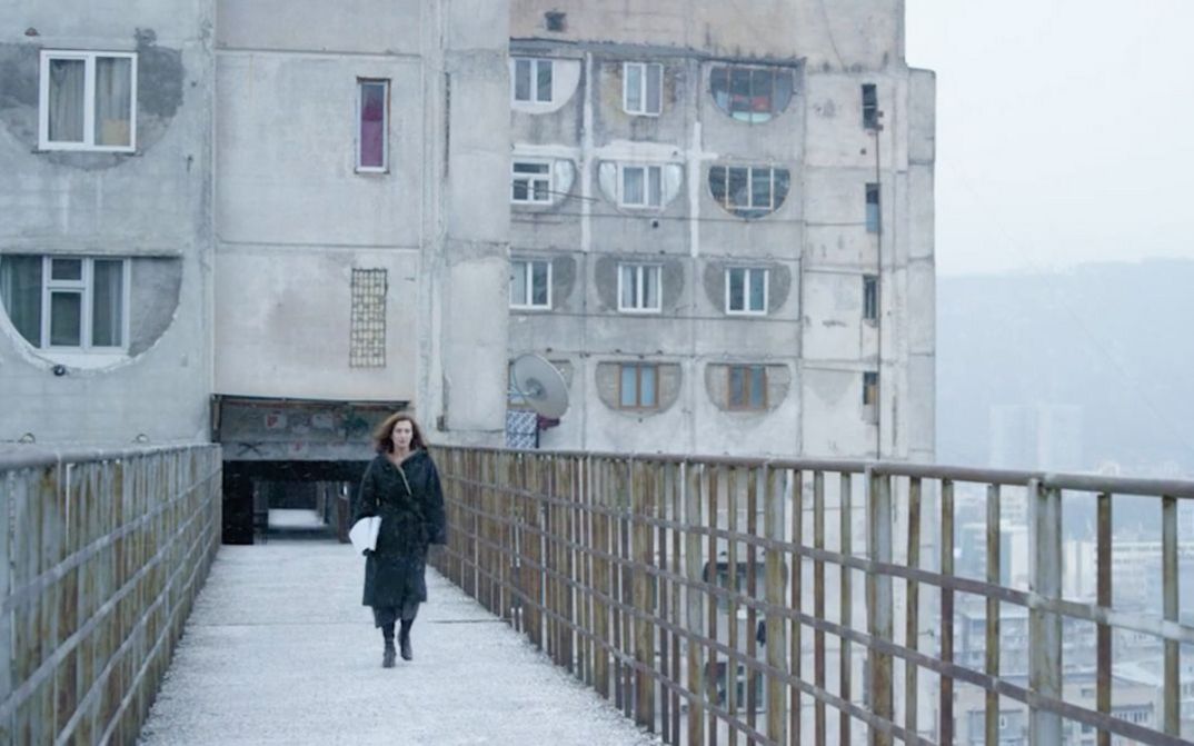 Filmstill aus SCARY MOTHER. Eine Frau läuft auf die Kamera zu, im Hintergrund ein großer Wohnblock.