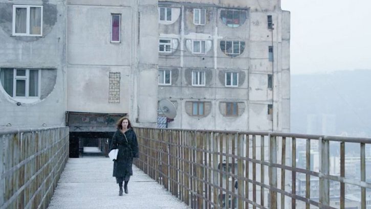 Filmstill aus SCARY MOTHER. Eine Frau läuft auf die Kamera zu, im Hintergrund ein großer Wohnblock.