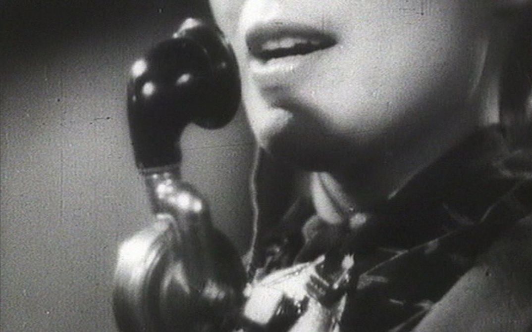 Filmstill aus ALLÔ BERLIN? ICI PARIS!: Das angeschnittende Gesicht einer Frau mit einem Telefonapparat.