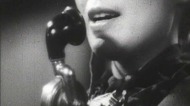 Film still from ALLÔ BERLIN? ICI PARIS!: The face of a woman with a telephone set.