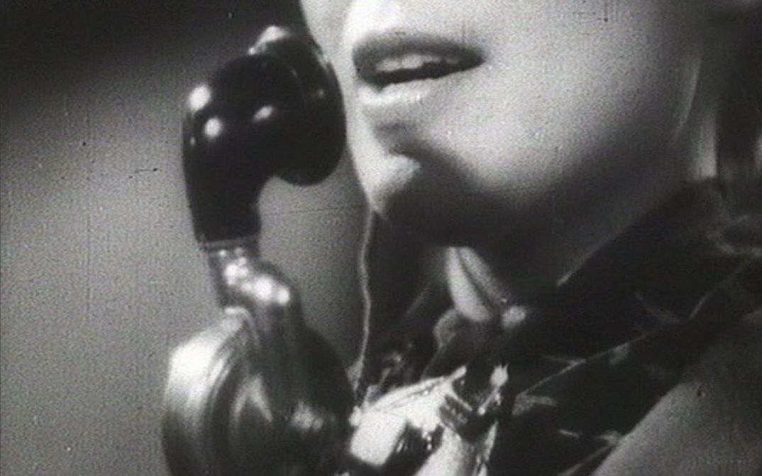 Film still from ALLÔ BERLIN? ICI PARIS!: The face of a woman with a telephone set.