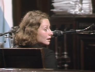 Still from the film "El juicio" by Ulises de la Orden. A woman is seated in a witness stand, looking to her right. A microfone is positioned next to her.