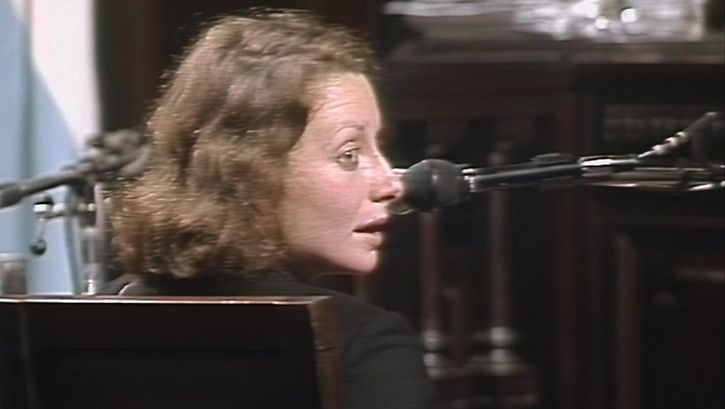 Still from the film "El juicio" by Ulises de la Orden. A woman is seated in a witness stand, looking to her right. A microfone is positioned next to her.