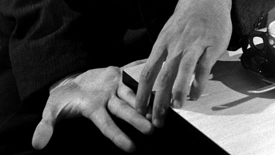 Filmstill aus PICKPOCKET: Zwei Hände berühren einander auf einem Tisch.