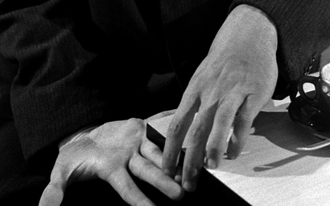 Filmstill aus PICKPOCKET: Zwei Hände berühren einander auf einem Tisch.