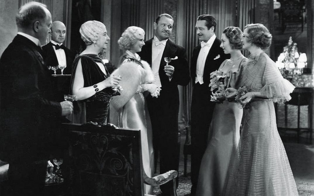 Filmstill aus DINNER AT EIGHT: Einige Menschen in Abendgarderobe stehen zusammen und halten Gläser in der Hand.