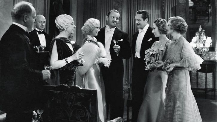 Film still from DINNER AT EIGHT: Some people in evening dress stand together and hold glasses in their hands.