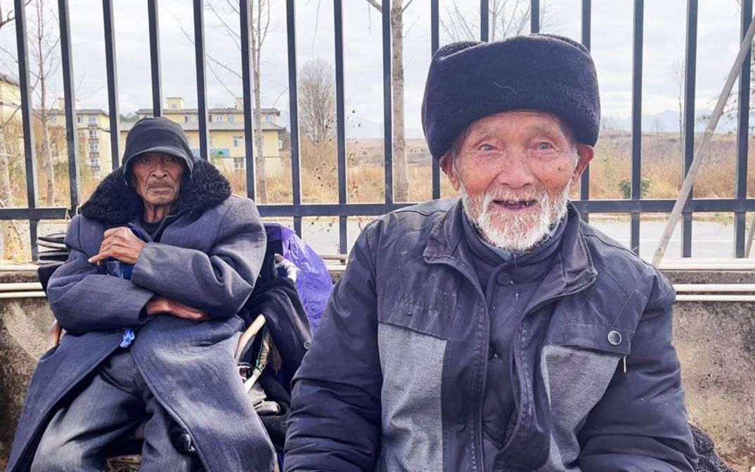 Film still from GUOCHANG by Nana Xu. The picture shows two elderly men in front of a fence.