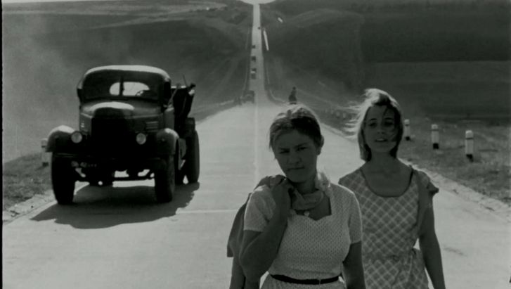Film still from BRIEF ENCOUNTERS: Two young women dressed in summer clothes are walking down a street. A lorry can be seen behind them.