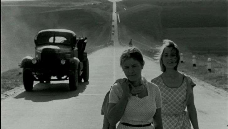 Film still from BRIEF ENCOUNTERS: Two young women dressed in summer clothes are walking down a street. A lorry can be seen behind them.