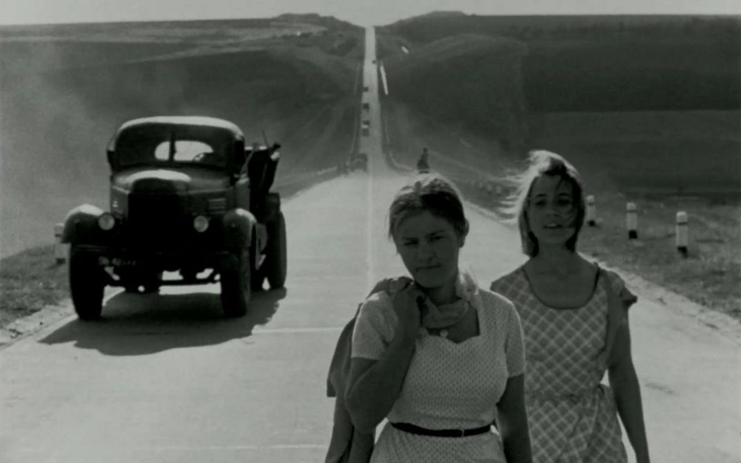 Filmstill auf BRIEF ENCOUNTERS: Zwei junge, sommerlich gekleidete Frauen gehen eine Straße entlang. Hinter ihnen ist ein Lastwagen zu sehen.