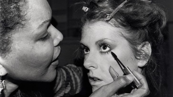 Film still from MODEL. A young woman is made up.