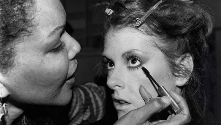 Film still from MODEL. A young woman is made up.