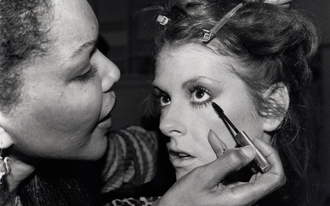 Film still from MODEL. A young woman is made up.