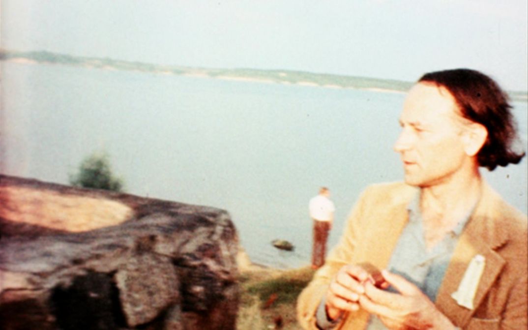 Film still from NOTES FOR JEROME. Jonas Mekas stands before a body of water.