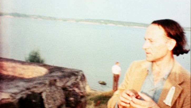Film still from NOTES FOR JEROME. Jonas Mekas stands before a body of water.