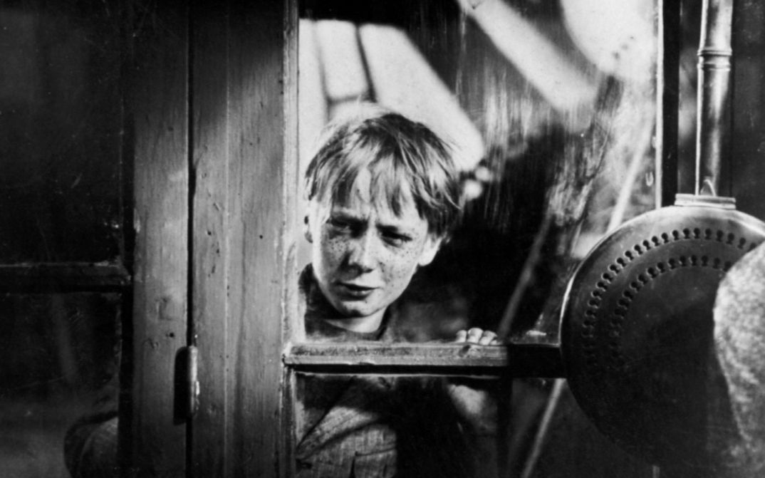 Film still from POIL DE CAROTTE: A boy with freckles looks through a window.