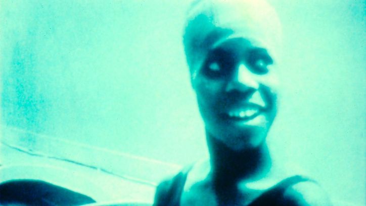 Film still from HANDTINTING: A monochrome turquoise picture of a laughing woman.