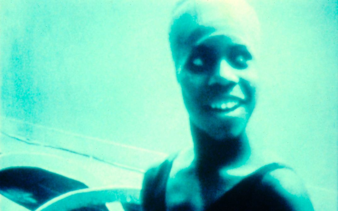 Film still from HANDTINTING: A monochrome turquoise picture of a laughing woman.