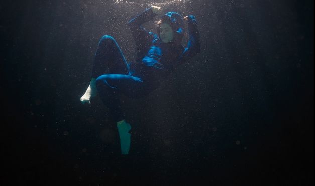 Person schwebt unter Wasser, Stoff und Luftblasen bewegen sich im Dunkeln.