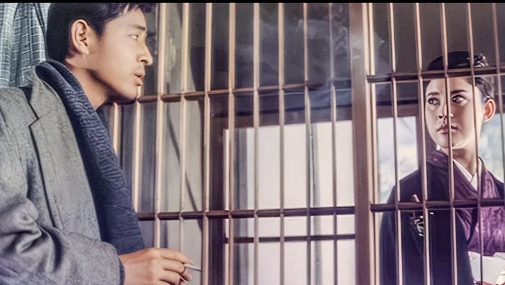 Film still from AKITSU SPRINGS: A man and a woman look at each other through a grille.