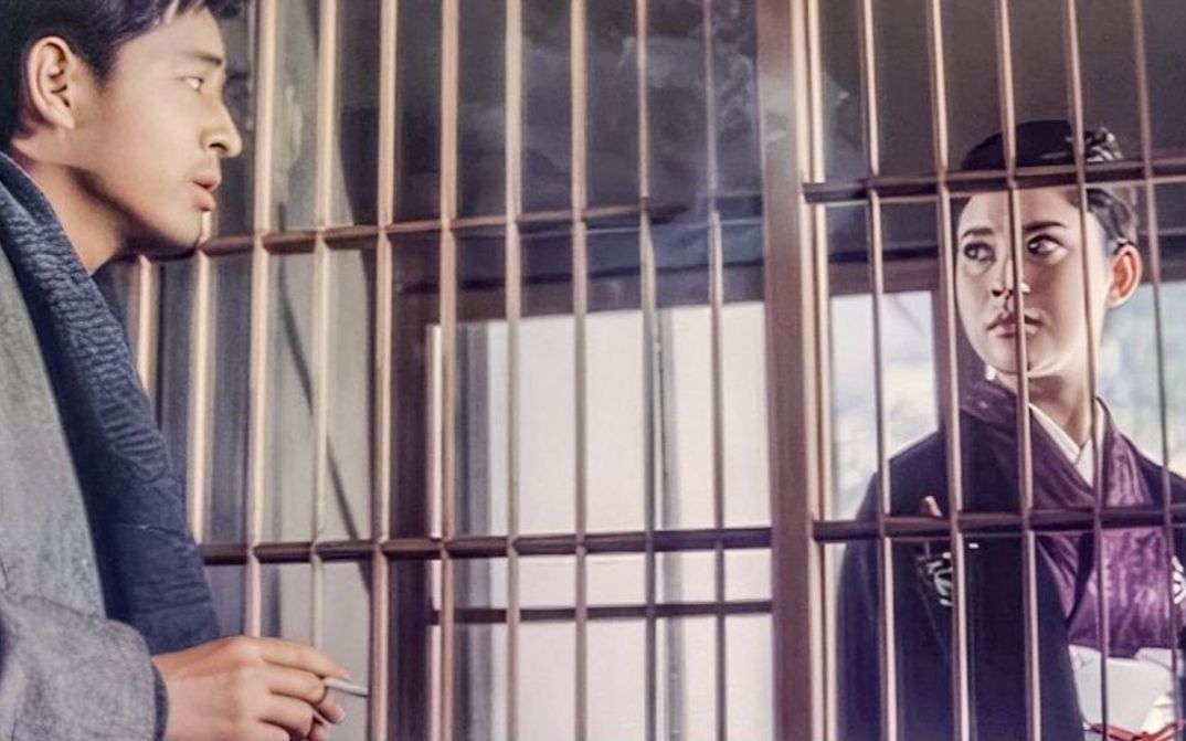 Filmstill aus AKITSU SPRINGS: Ein Mann und eine Frau blicken sich durch ein Gitter hindurch an.