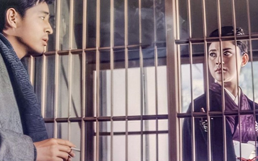 Film still from AKITSU SPRINGS: A man and a woman look at each other through a grille.