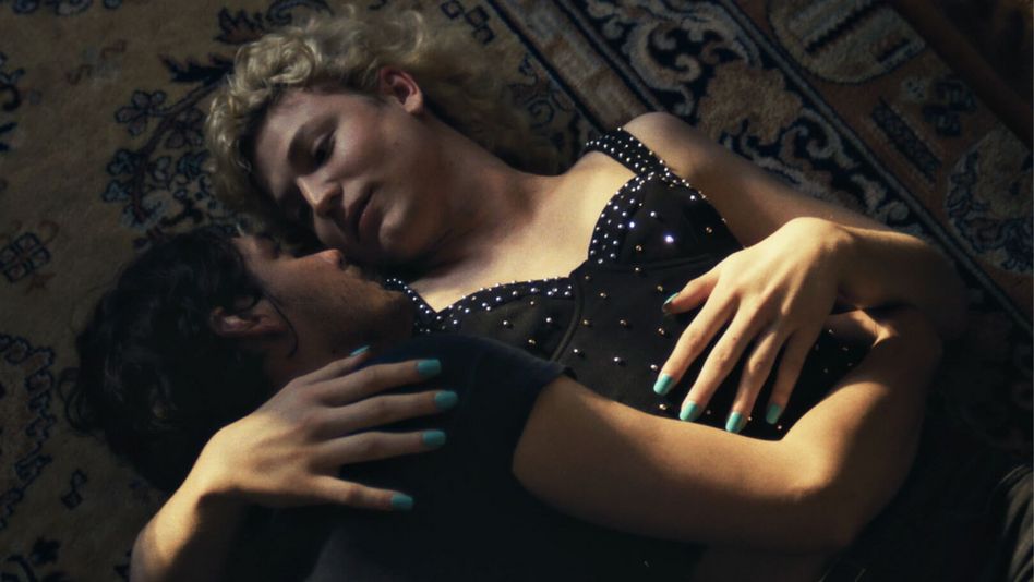 Filmstill aus BIS ANS ENDE DER NACHT: Zwei Menschen liegen angezogen in einer Umarmung auf dem Boden und blicken sich in die Augen.