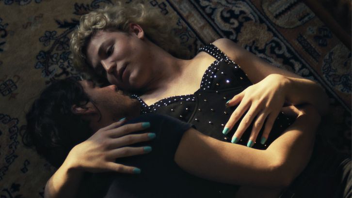 Filmstill aus BIS ANS ENDE DER NACHT: Zwei Menschen liegen angezogen in einer Umarmung auf dem Boden und blicken sich in die Augen.