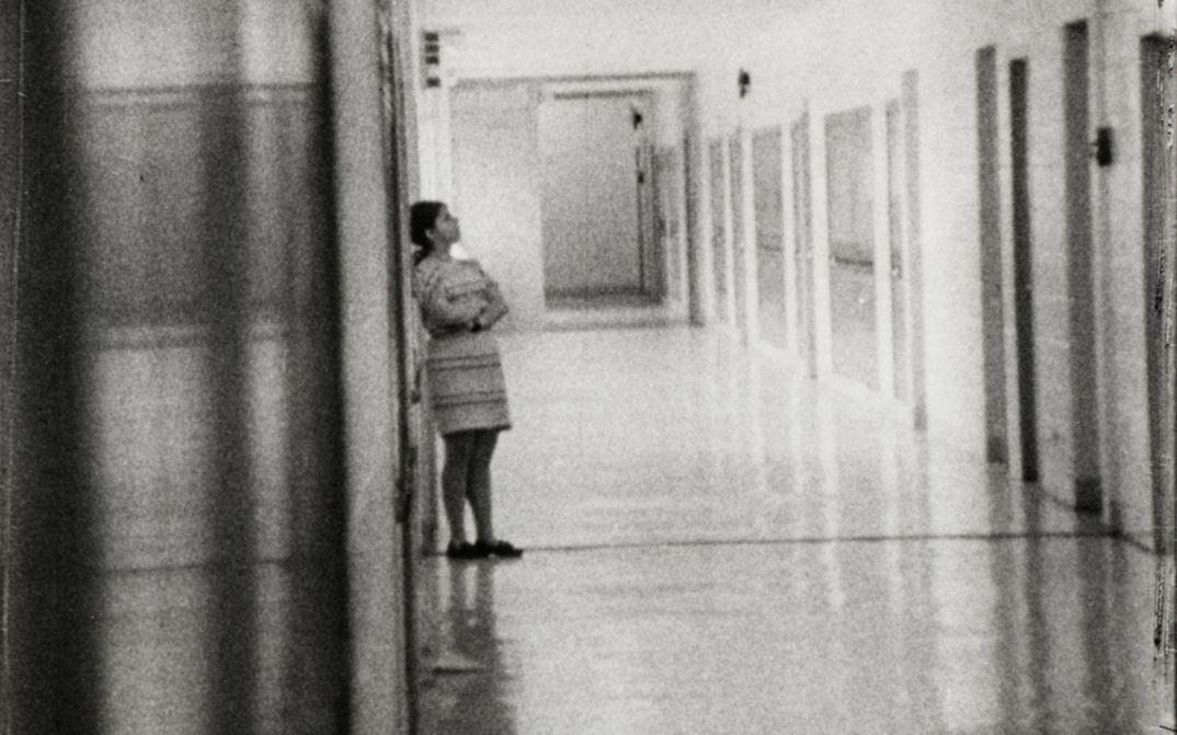 Filmstill aus HIGH SCHOOL. Aufnahme eines langen Flurs in einem Schulgebäude, eine Person ist an eine Wand gelehnt.