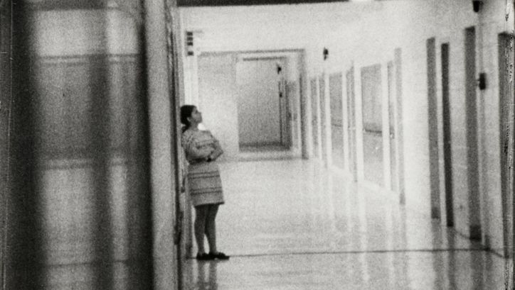 Filmstill aus HIGH SCHOOL. Aufnahme eines langen Flurs in einem Schulgebäude, eine Person ist an eine Wand gelehnt.