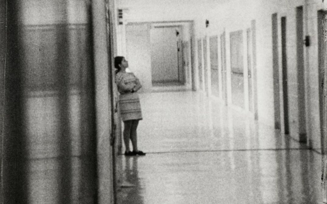 Film still from HIGH SCHOOL. Shot of a long hallway in a school building, a person is leaning against a wall.