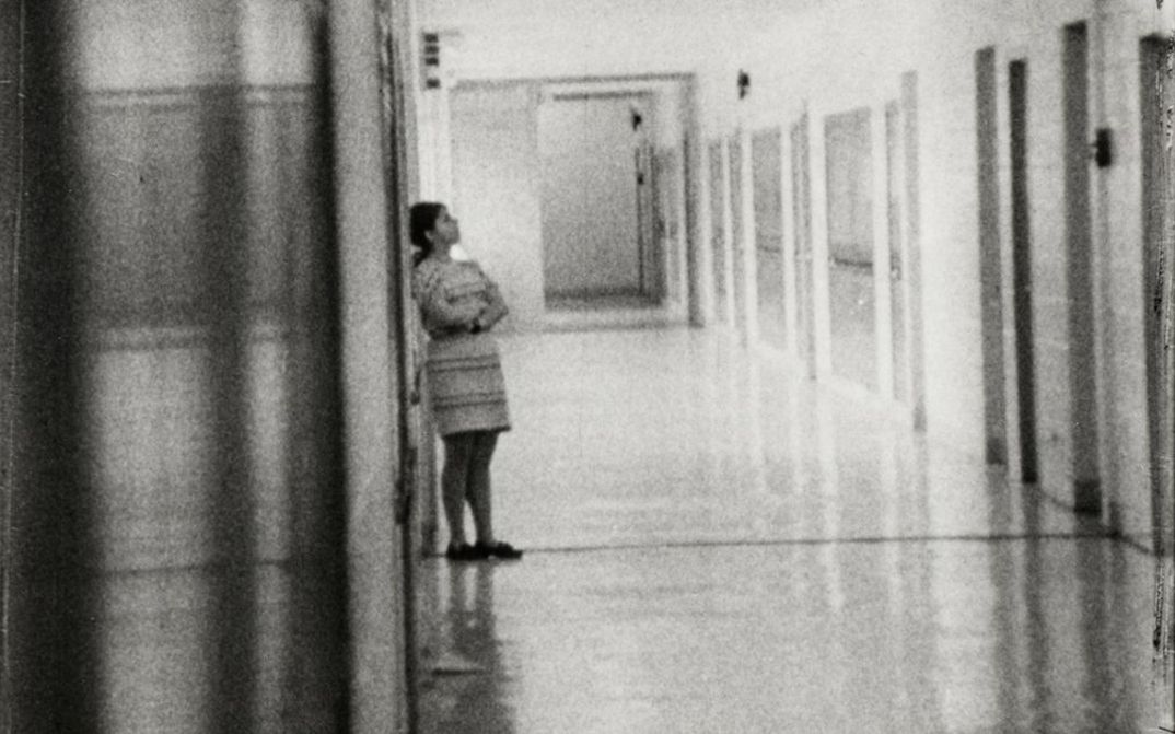Filmstill aus HIGH SCHOOL. Aufnahme eines langen Flurs in einem Schulgebäude, eine Person ist an eine Wand gelehnt.
