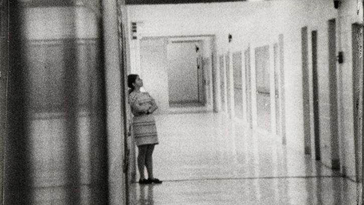 Film still from HIGH SCHOOL. Shot of a long hallway in a school building, a person is leaning against a wall.