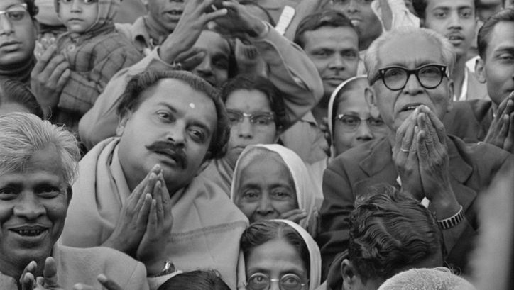 Filmstill aus MAHAPURUSH: Menschen stehen dicht beieinander, blicken nach oben und halten die Hände teils aneinander.