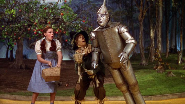 Filmstill aus THE WIZARD OF OZ: Judy Garland als Dorothy neben dem Zinnmann und der Vogelscheuche.