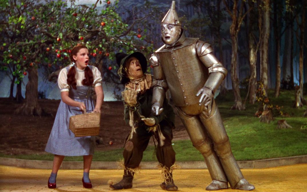 Film still from THE WIZARD OF OZ: Judy Garland as Dorothy next to the Tin Man and the Scarecrow.